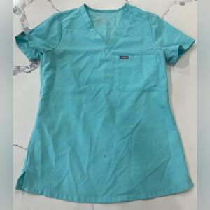 Light blue/teal Figs scrub set with small pen stains on shirt.